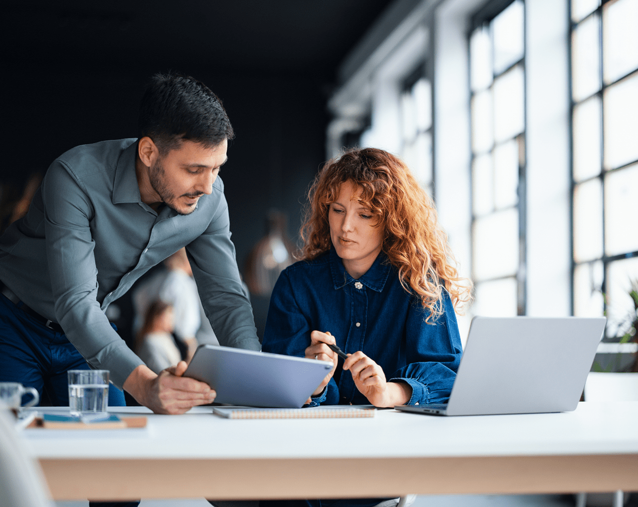Business professionals reviewing documents together on a tablet in a modern office workspace.